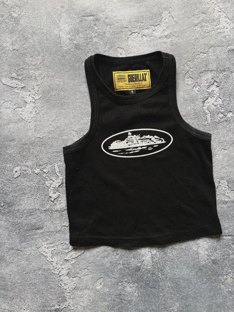 Może przedstawiać: Czarny tank top z białym nadrukiem budynku w owalu. Tank top ma prążkowaną fakturę i małą metkę z napisem "GUERILLAZ". Tank top jest w rozmiarze S.