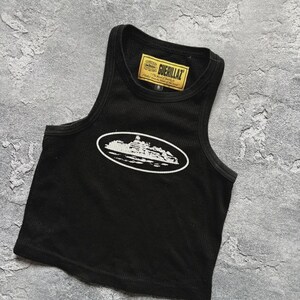 Może przedstawiać: Czarny top z białym owalnym nadrukiem przedstawiającym zarys budynku. Top ma prążkowaną fakturę i małą ż&oacute;łtą metkę z napisem "GUERILLAZ". Top jest w rozmiarze S.