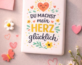 May include: A white rectangular magnet with the German phrase "DU MACHST mein HERZ glücklich" (You make my heart happy) in colorful lettering. The magnet is decorated with hearts, flowers, and a smiling sun. Other decorative magnets are also visible.