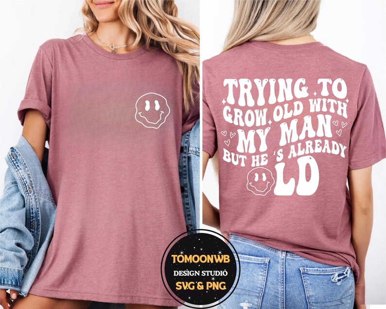 May include: A mauve-colored t-shirt with a white smiley face graphic on the front and the text "TRYING TO GROW OLD WITH MY MAN BUT HE'S ALREADY OLD" on the back. The shirt is a casual style.