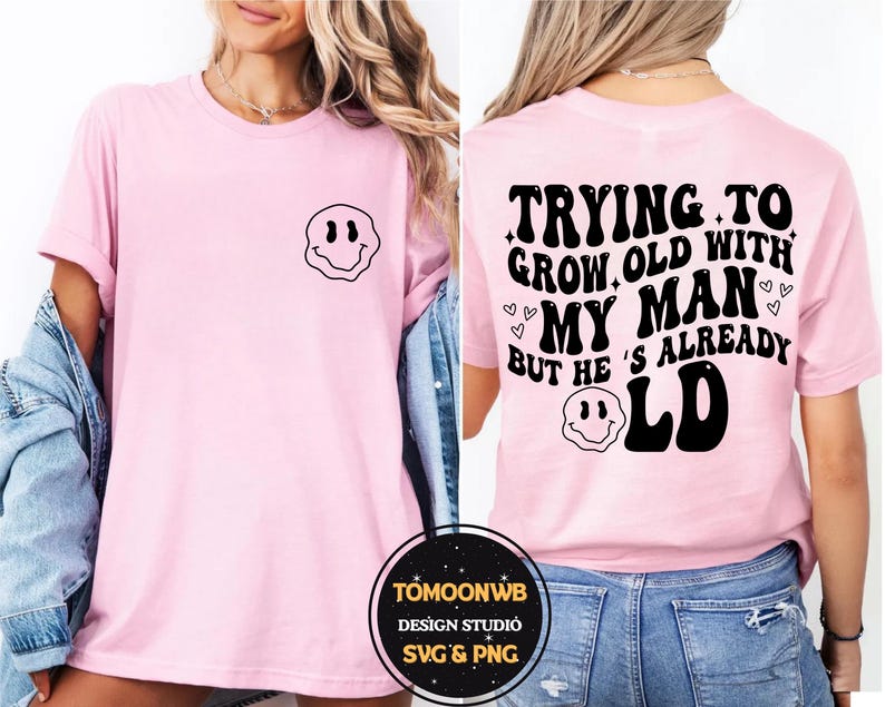 May include: A light pink t-shirt with a black smiley face graphic on the front and the text "TRYING TO GROW OLD WITH MY MAN BUT HE'S ALREADY OLD" on the back. The shirt is a casual style.