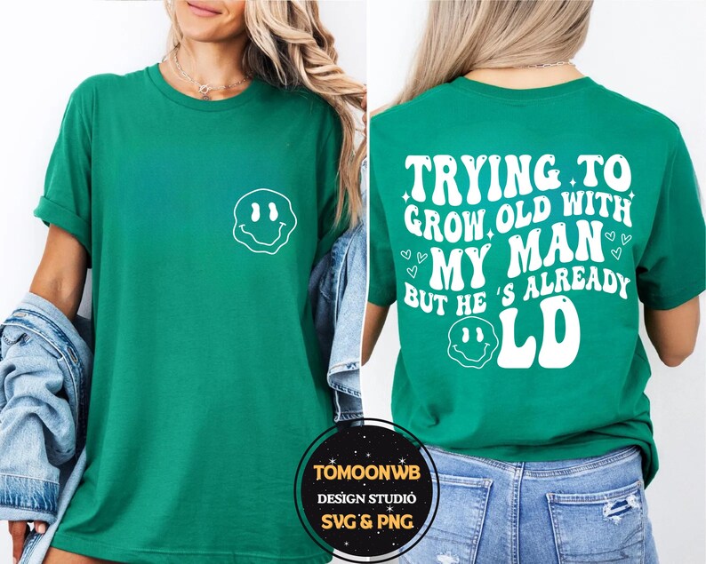 May include: Green t-shirt with a white smiley face graphic on the front. The back of the shirt features the text "TRYING TO GROW OLD WITH MY MAN BUT HE'S ALREADY OLD" in a retro font. A casual, unisex tee.