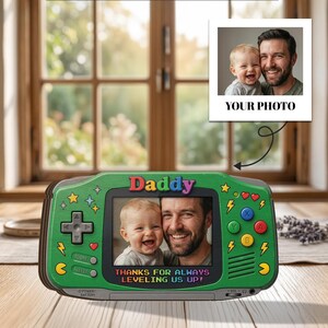 May include: Green handheld game console-shaped photo frame with the word "Daddy" at the top. The frame displays a photo of a man and a baby. Text at the bottom reads "THANKS FOR ALWAYS LEVELING US UP!" A separate photo is attached.