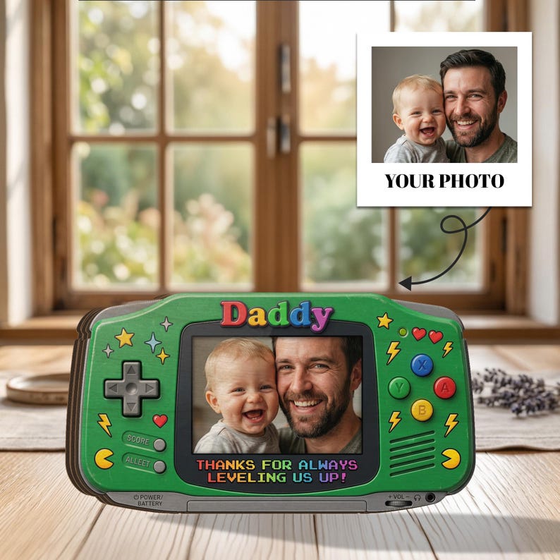 May include: Green handheld game console-shaped photo frame with the word "Daddy" at the top. The frame displays a photo of a man and a baby. Text at the bottom reads "THANKS FOR ALWAYS LEVELING US UP!" A separate photo is attached.