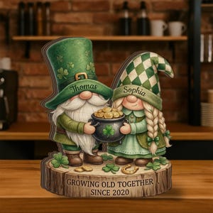 May include: A wooden St. Patrick's Day decoration featuring two gnomes, one with a green hat and the name "Thomas", the other with a green and white checkered hat and the name "Sophia". They hold a pot of gold. The base reads "GROWING OLD TOGETHER SINCE 2020".