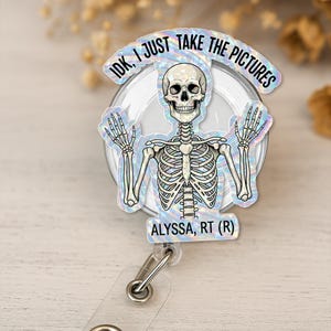 May include: A holographic badge reel with a cartoon skeleton and the text "IDK, I JUST TAKE THE PICTURES." The badge also includes the text "ALYSSA, RT (R)." The reel has a clear plastic strap and a metal clip.