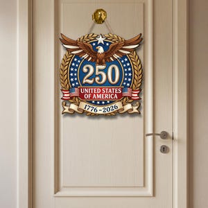 K&ouml;nnte beinhalten: Ein dekorativer Wandbehang mit einem Wei&szlig;kopfseeadler mit ausgebreiteten Fl&uuml;geln &uuml;ber der Zahl 250, dem Text UNITED STATES OF AMERICA und den Jahren 1776-2026. Das Design umfasst einen blauen Hintergrund mit wei&szlig;en Sternen, goldenen Lorbeerbl&auml;ttern und roten Akzenten.