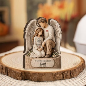 Könnte beinhalten: Eine hölzerne Gedenkfigur eines Engels mit einem Kind, mit gravierten Flügeln und dem Text "IN LOVING MEMORY OF Dad 1978-2026". Der Engel und das Kind haben rote Herzakzente. Das Kleid des Kindes trägt den Text "Your Wings Were Ready But My Heart Was Not".