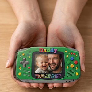 May include: A green handheld game console-shaped photo frame with the word "Daddy" at the top. The frame displays a photo of a man and a child. The text "THANKS FOR ALWAYS LEVELING US UP!" is below the photo.