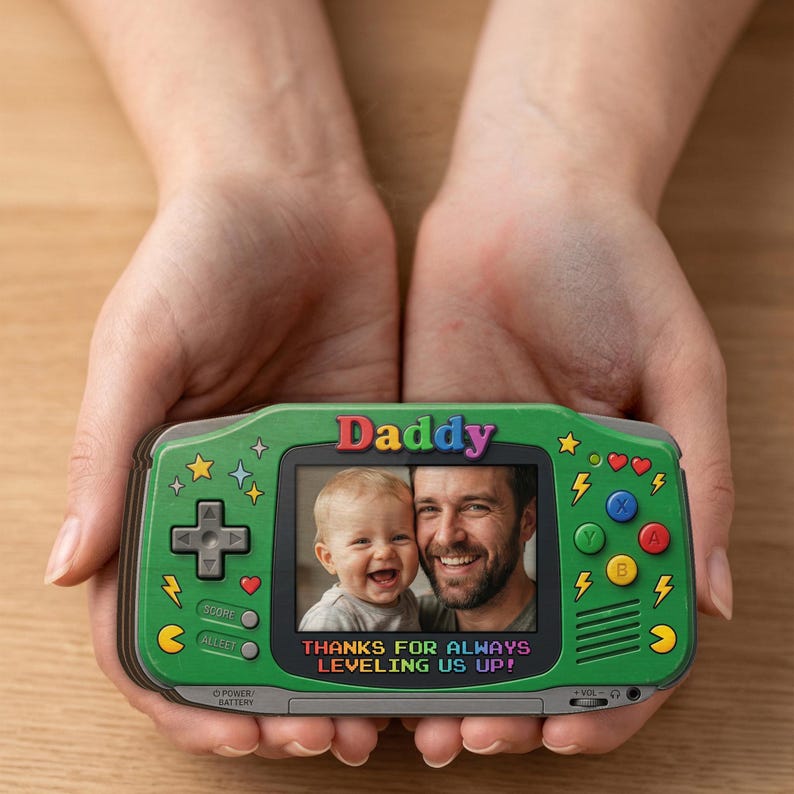 May include: A green handheld game console-shaped photo frame with the word "Daddy" at the top. The frame displays a photo of a man and a child. The text "THANKS FOR ALWAYS LEVELING US UP!" is below the photo.