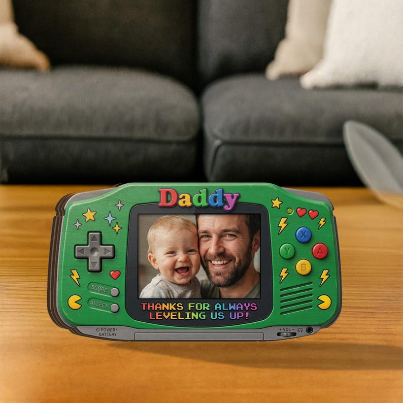 May include: Green handheld game console-shaped photo frame with the word "Daddy" in colorful letters. The frame displays a photo of a father and child. Text reads "THANKS FOR ALWAYS LEVELING US UP!"