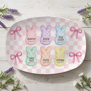 May include: An oval-shaped Easter serving platter with a pink and white checkered pattern. It features six pastel-colored bunny shapes with inspirational words and Bible verses. Pink bows are placed around the edges.