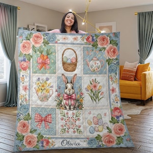 May include: A pastel Easter-themed quilt with a patchwork design. It features squares with carrots, Easter baskets, teapots, flowers, and a bunny with a pink bow. The quilt is decorated with floral borders. The name "Olivia" is printed at the bottom.