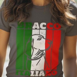Può includere: Maglietta grigia con illustrazione di un cane Bracco Italiano. Il design incorpora i colori della bandiera italiana: verde, bianco e rosso. Le parole "BRACCO" e "ITALIA" sono stampate.
