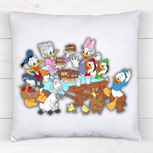 Peut inclure: Coussin carr&eacute; blanc avec une sc&egrave;ne de dessin anim&eacute; color&eacute;e de personnages Disney. Donald Duck, Daisy Duck et d'autres personnages sont r&eacute;unis autour d'une table avec un g&acirc;teau, une ch&egrave;vre, des poulets et un panier de fruits.