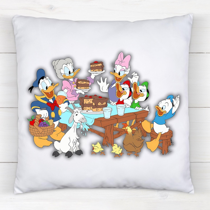 Peut inclure: Coussin carr&eacute; blanc avec une sc&egrave;ne de dessin anim&eacute; color&eacute;e de personnages Disney. Donald Duck, Daisy Duck et d'autres personnages sont r&eacute;unis autour d'une table avec un g&acirc;teau, une ch&egrave;vre, des poulets et un panier de fruits.