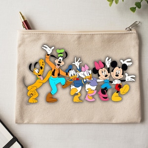Peut inclure: Une pochette zipp&eacute;e en toile beige avec un graphisme color&eacute; des personnages Disney Pluto, Dingo, Donald Duck, Daisy Duck, Minnie Mouse et Mickey Mouse. Les personnages sont align&eacute;s, les bras lev&eacute;s en signe de c&eacute;l&eacute;bration.