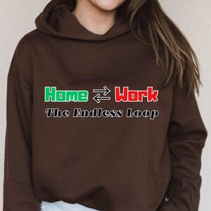 Puede incluir: Una sudadera con capucha marrón con el texto "Home ↔ Work The Endless Loop" en verde y rojo. La sudadera es de color liso y tiene una capucha con cordón.
