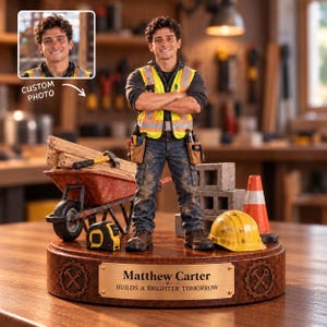 Könnte beinhalten: Eine individuelle Bauarbeiter-Figur mit verschränkten Armen, die eine Warnweste und Arbeitsstiefel trägt. Der Sockel zeigt eine Plakette mit der Aufschrift Matthew Carter BUILDS A BRIGHTER TOMORROW, eine Schubkarre, ein Maßband und einen Helm.