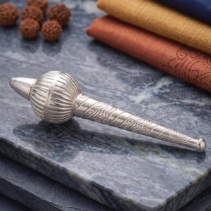 May include: A silver-toned mace-shaped object featuring a rounded, ribbed head and a tapered handle decorated with intricate, swirling engraved patterns. The item has a polished, metallic finish and a pointed tip at the top of the rounded section.