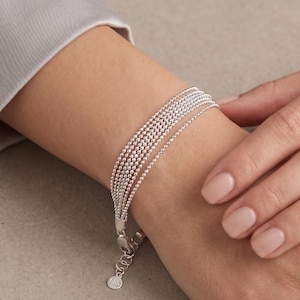 May include: A multi-strand bracelet composed of five delicate silver ball chains. The bracelet features a polished metallic finish and includes an adjustable extender chain with a small round tag stamped with the number 925 for sterling silver.