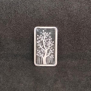 May include: A rectangular silver bar with a detailed tree design. The tree has a thick trunk, branches, and numerous leaves. The bar is set against a dark background.
