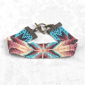 May include: A beaded bracelet with a geometric pattern in shades of pink, blue, and white. The bracelet has a brass clasp.