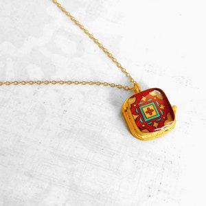 May include: Gold chain necklace with a square pendant featuring a colorful geometric design. The pendant has a red, yellow, blue, and green pattern.