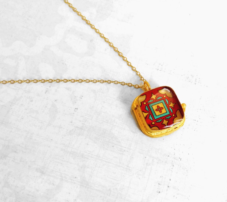 May include: Gold chain necklace with a square pendant featuring a colorful geometric design. The pendant has a red, yellow, blue, and green pattern.