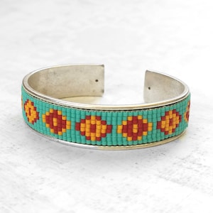 May include: A silver bangle bracelet with a turquoise and red beaded design featuring a repeating pattern of yellow and red circles.
