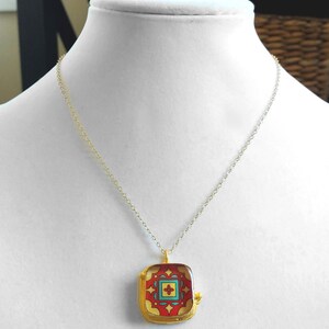May include: A gold chain necklace with a square pendant featuring a colorful geometric design. The pendant has a red, yellow, blue, and green pattern.