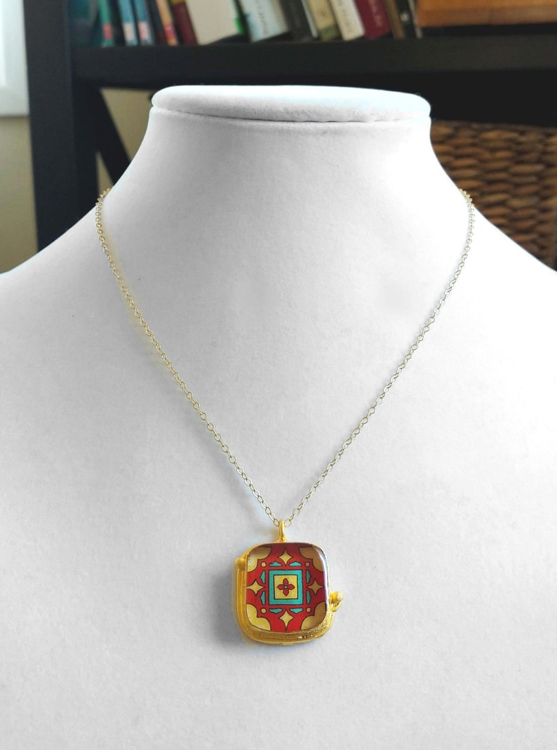 May include: A gold chain necklace with a square pendant featuring a colorful geometric design. The pendant has a red, yellow, blue, and green pattern.