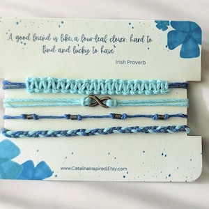May include: A set of five blue friendship bracelets displayed on a card with an Irish proverb about friendship. The bracelets feature various designs, including macrame, infinity symbol, and braided styles. The card has blue floral accents and the website address www.Catalinainspired.Etsy.com.