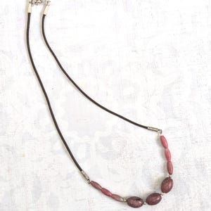 May include: A simple necklace with a brown leather cord and a row of pink and white oval-shaped gemstone beads.
