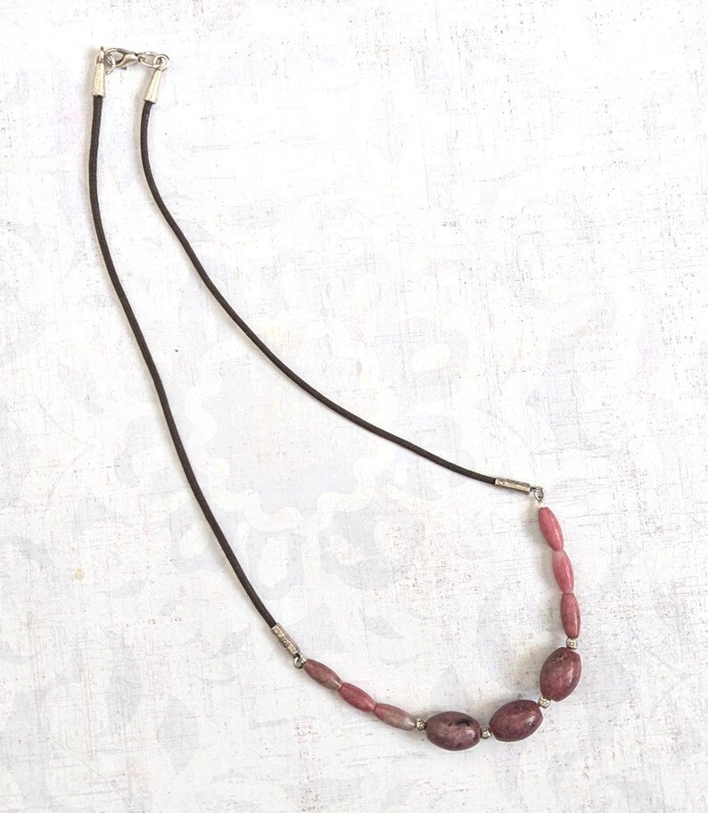 May include: A simple necklace with a brown leather cord and a row of pink and white oval-shaped gemstone beads.