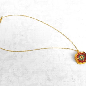May include: A gold chain necklace with a square pendant featuring a red, green, and yellow geometric pattern.