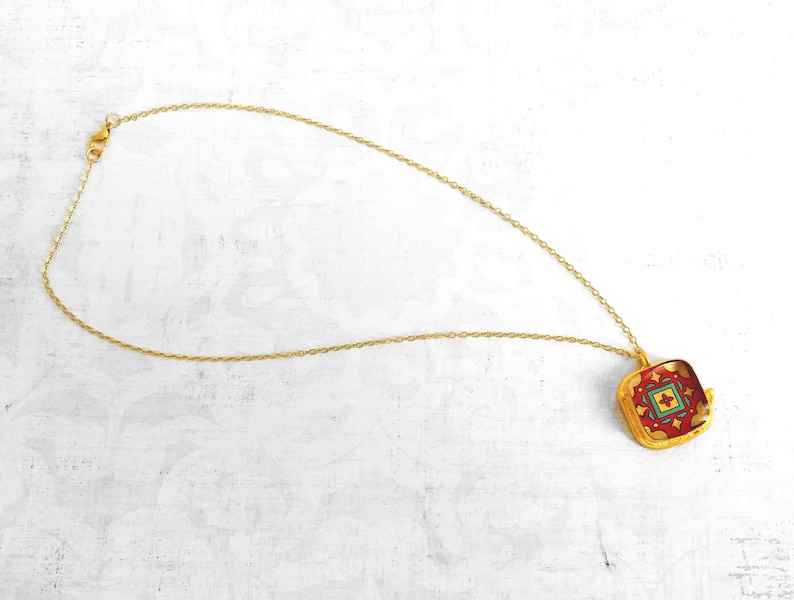 May include: A gold chain necklace with a square pendant featuring a red, green, and yellow geometric pattern.