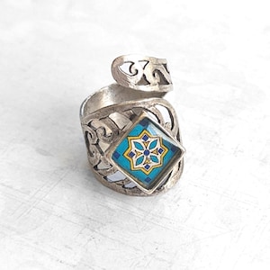 May include: A silver ring with an intricate design and a blue and yellow tile-like inlay.