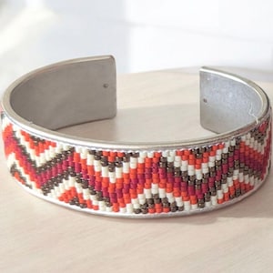 May include: A silver cuff bracelet with a geometric pattern of red, orange, white, and brown beads.