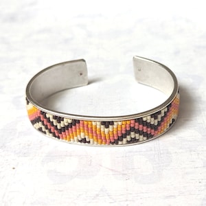 May include: A silver bangle bracelet with a beaded design in shades of pink, orange, white, and black.