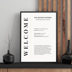May include: A framed sign with the text "WELCOME" on the left side and information about "THE AESTHETIC RETREAT" on a white background. The sign is on a black surface with decorative vases and a wooden wall in the background.