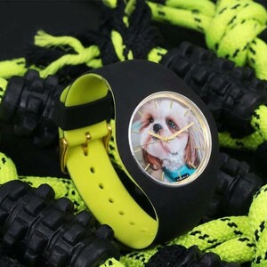May include: Black wristwatch with a yellow band and a gold buckle. The watch face features a photo of a Shih Tzu dog. The watch is surrounded by black and neon green dog toys.