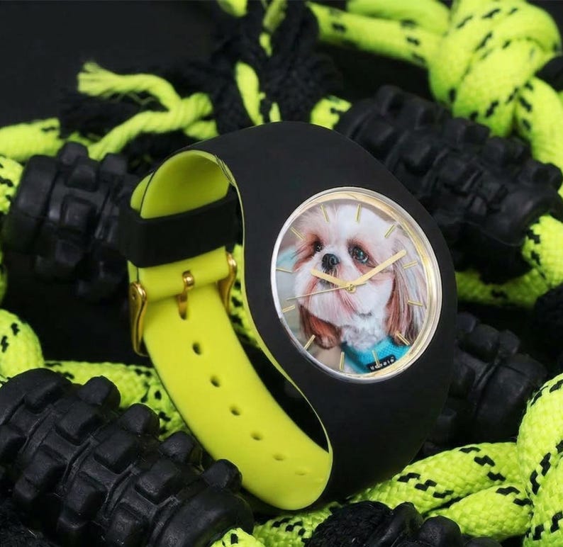 May include: Black wristwatch with a yellow band and a gold buckle. The watch face features a photo of a Shih Tzu dog. The watch is surrounded by black and neon green dog toys.
