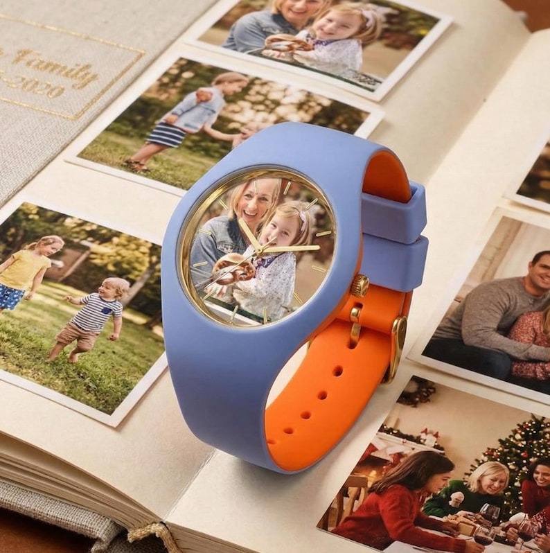 May include: A blue and orange wristwatch with a photo inside the watch face, resting on an open photo album. The watch has a blue band and an orange strap. Family photos surround the watch.