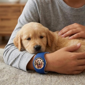 May include: A blue wristwatch with a white band features a photo of a golden retriever. The watch is on a person's wrist, with a golden retriever puppy resting on their arm. The puppy has light brown fur.