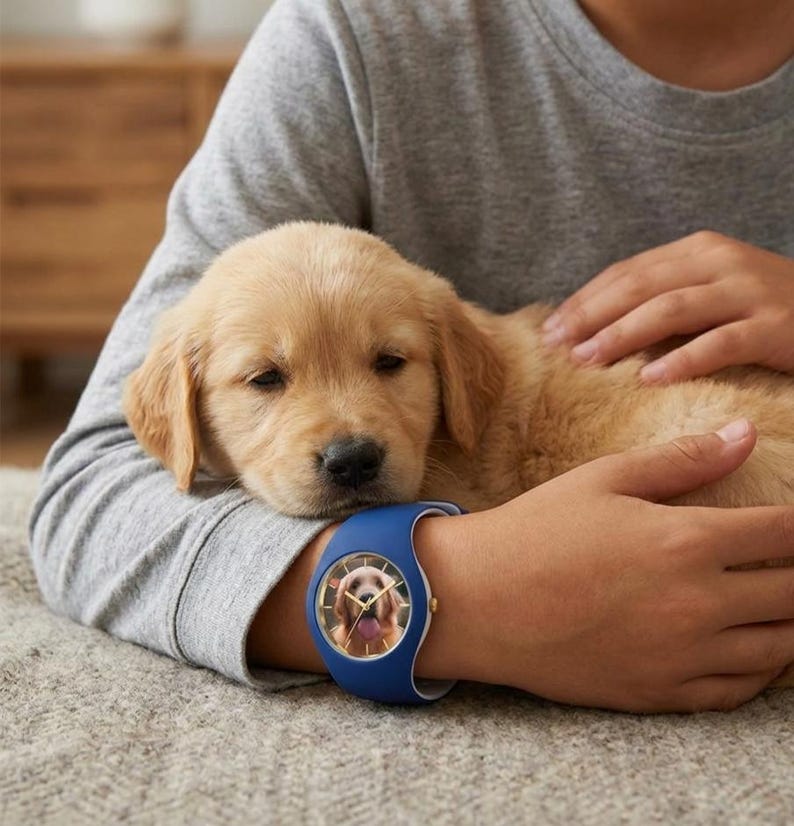 May include: A blue wristwatch with a white band features a photo of a golden retriever. The watch is on a person's wrist, with a golden retriever puppy resting on their arm. The puppy has light brown fur.