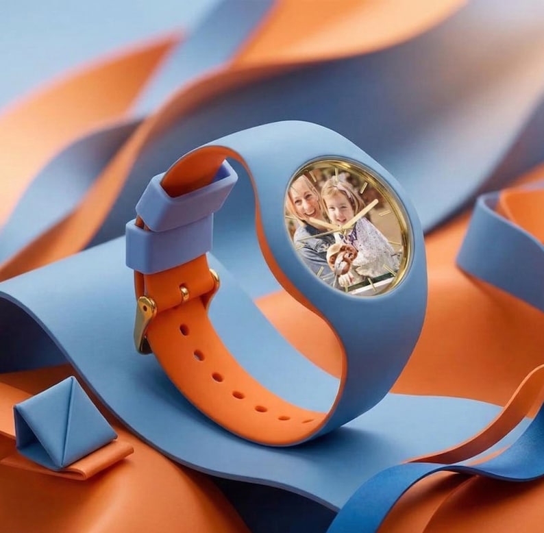May include: A blue and orange wristwatch with a gold-colored watch face. The watch face displays a photograph of two people. The watch band is blue and orange, with a gold buckle. The watch is displayed on a blue and orange background.