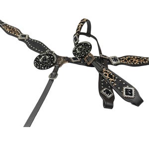May include: A black and leopard print horse breast collar with silver accents. The breast collar features a decorative design with rhinestones and a circular emblem with the text "HORSE & PET INTERNATIONAL".