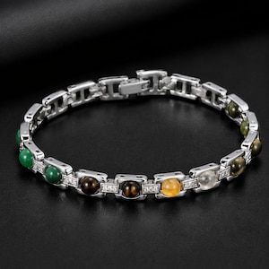 May include: Silver-toned bracelet featuring a series of colorful gemstone beads, including green, brown, yellow, and clear stones. The bracelet has a rectangular link design with small, clear accent stones.