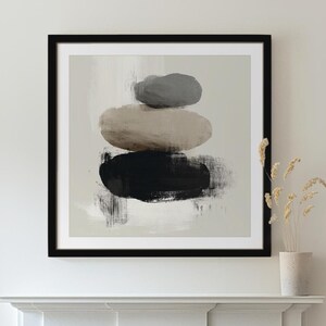 May include: Abstract art print featuring a stack of three stones in shades of gray, beige, and black. The artwork is framed in a black frame and hangs above a white fireplace. The room also includes a modern chair and a floor lamp.